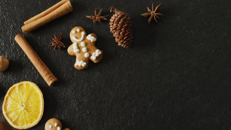 video of smiling gingerbread men and spices, slices of orange and nuts over black background