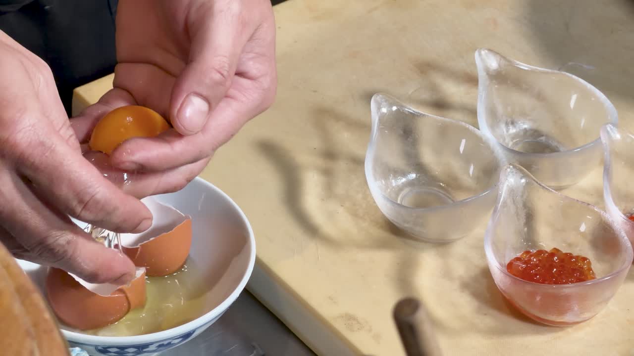 Professional chef carefully separates egg yolk beside glass bowls of bright fish roe