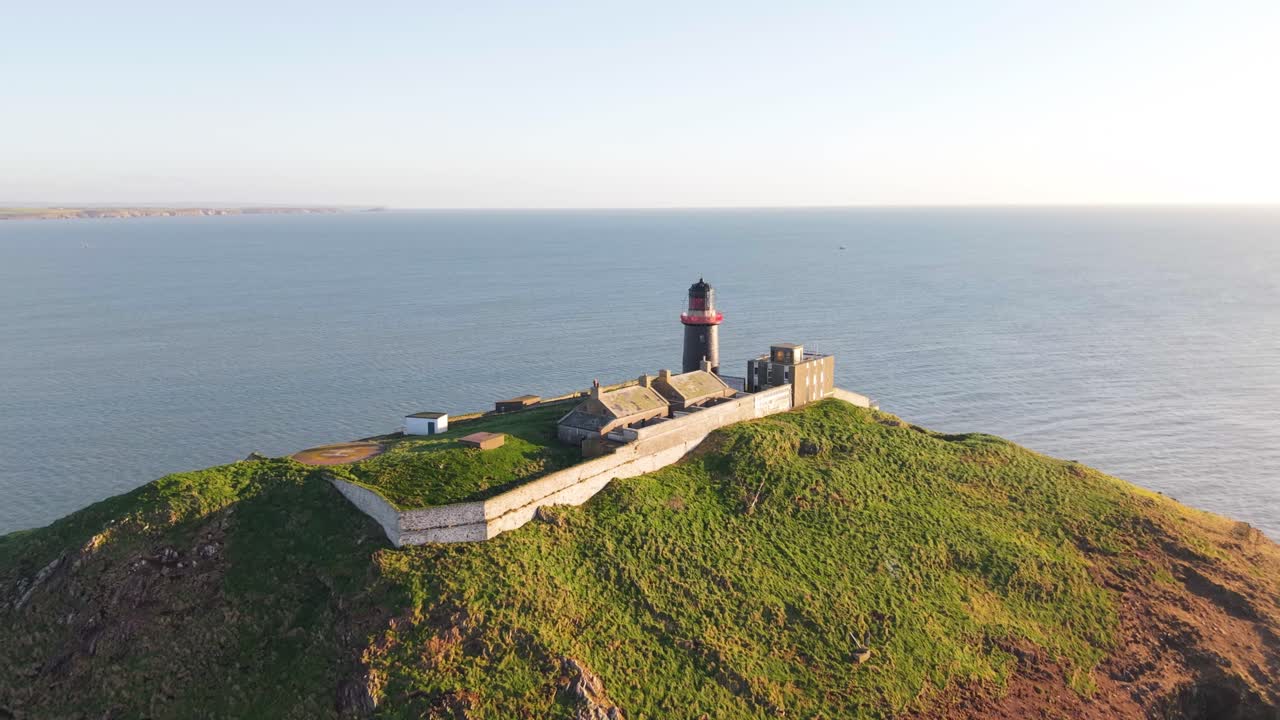 Ballycotton Lighthouse on a grassy cliff overlooking the ocean in sunny County Cork