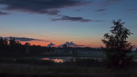 Clouds-streak-to-over-dam-in-woods,-orange-horizon-at-dawn