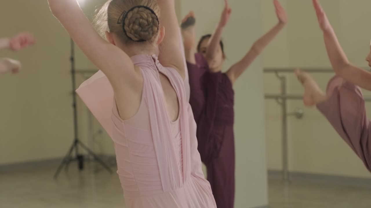 группа молодых студентов балета в черной танцевальной одежде практикует позиции в просторной балетной студии с деревянным полом и настенными решетками. сосредоточенные выражения и синхронизированные движения.