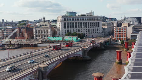 Vista-Aérea-Del-Tráfico-Del-Puente-Sobre-El-Río-Támesis.-Seguimiento-De-Un-Par-De-Típicos-Coches-Rojos-De-Dos-Pisos-Conduciendo-Por-El-Puente-Blackfriars.-Londres,-Reino-Unido