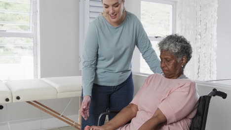 Fisioterapeuta-Femenina-Caucásica,-Mujer-Afroamericana-Mayor-En-Silla-De-Ruedas-Haciendo-Ejercicio,-Cámara-Lenta