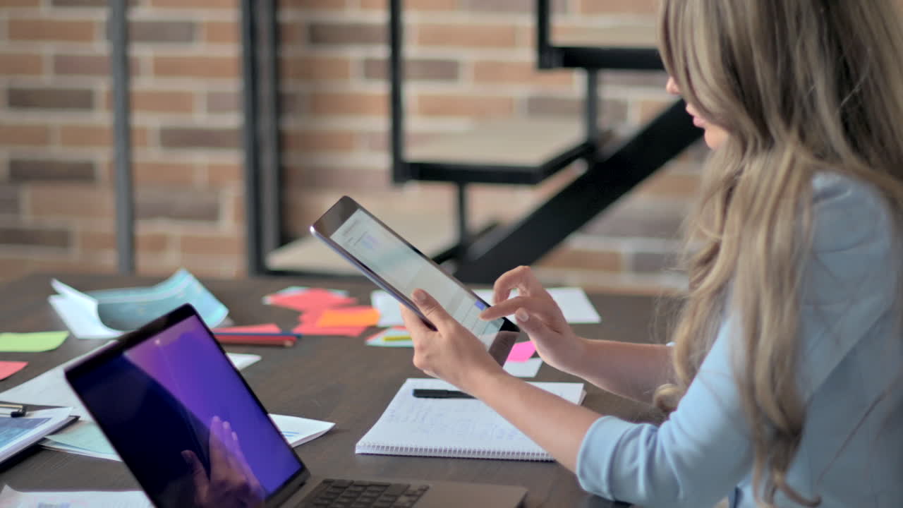 Mulher de blazer azul trabalhando em um tablet em uma mesa em um escritório
