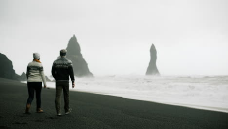 couple walking on a black sand beach in iceland