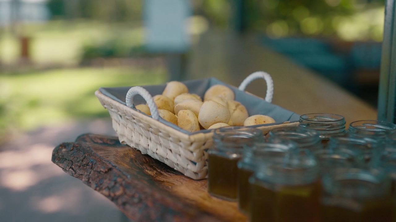 Piccoli panini al formaggio, chipá, sono serviti accanto a brocche di mate cocido, una bevanda calda, in un cesto di vimini su un tavolo di legno all'aperto, creando una scena rustica e invitante.