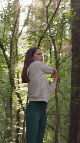 joven atleta estira los brazos en el bosque. jugando deportes rodeado de diferentes tipos de árboles en la naturaleza en un clima soleado. los rayos del sol caen sobre la dama