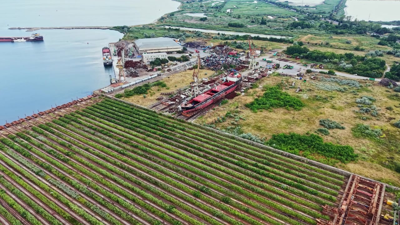 Schiffbau am Wasser mit einer großen Fläche für Schiffsteile und angrenzende Strukturen bei Tageslicht.