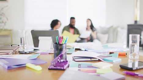 busy desk and diverse friends working together on couch in background, in slow motion