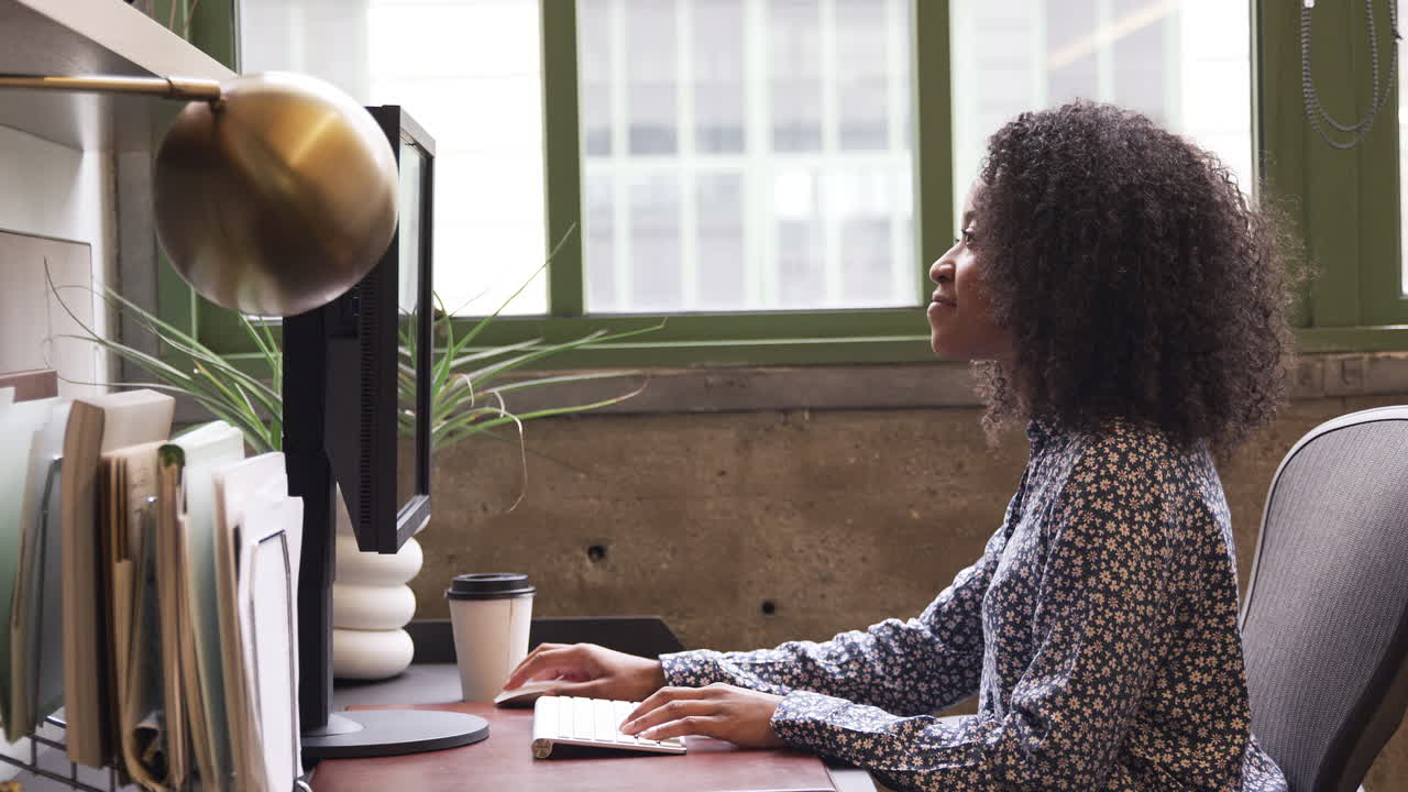 Young black woman using computer in an office, side view