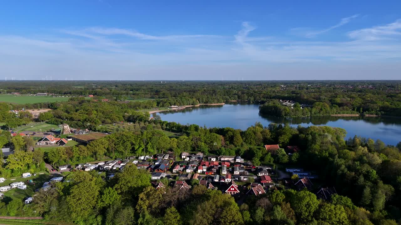 Campground and campsite with natural lake and windmill in the Netherlands. Aerial lateral wide shot. Sunset time in the evening. Panorama wide shot. Blue sky in summer.