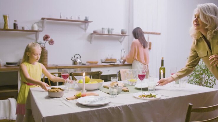 Mother, Daughter And Grandmother Removing The Plates From The Table After Family Dinner