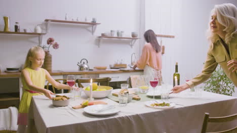 mother, daughter and grandmother removing the plates from the table after family dinner