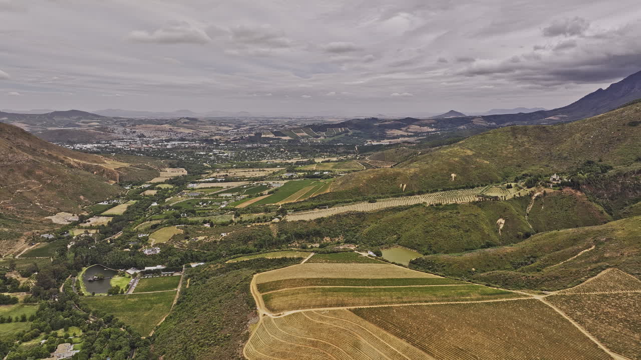 Stellenbosch South Africa Aerial v25 flyover capturing a lush green valley featuring vineyard estates, rolling hills, and a distant town under a cloudy sky - Shot with Mavic 3 Pro Cine - Jan 6th 2024