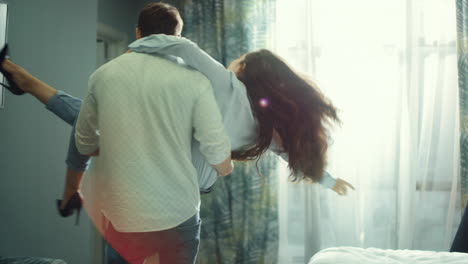 Young-couple-hugging-in-hotel-room.-Man-carrying-woman-in-hands-indoors.