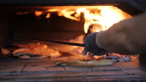 chef uses long pizza peel to move pizzas inside traditional wood fire oven