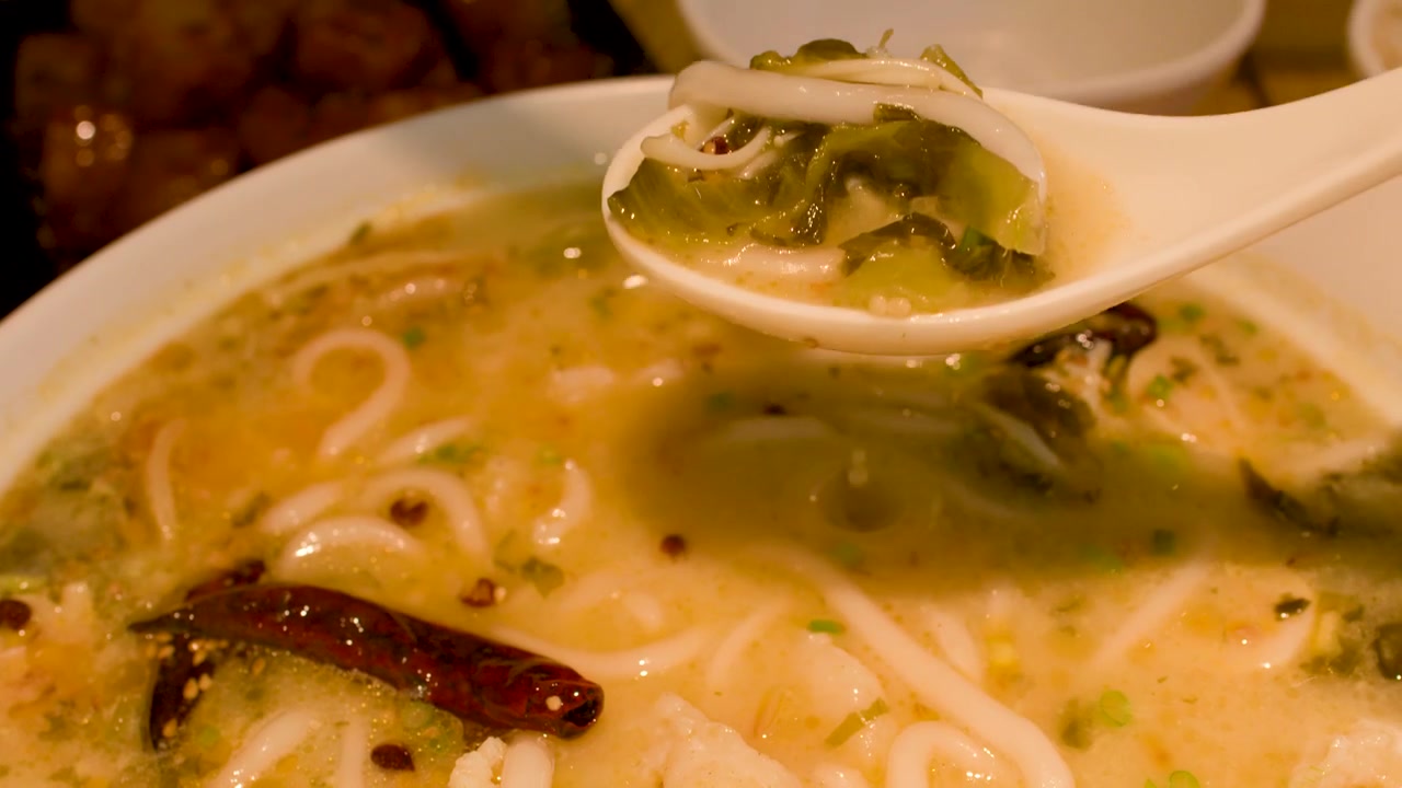 Primo piano di spaghetti di riso e brodo piccante sollevati con un cucchiaio di ceramica