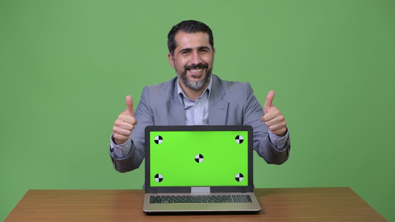 Handsome Persian bearded businessman showing laptop and giving thumbs up