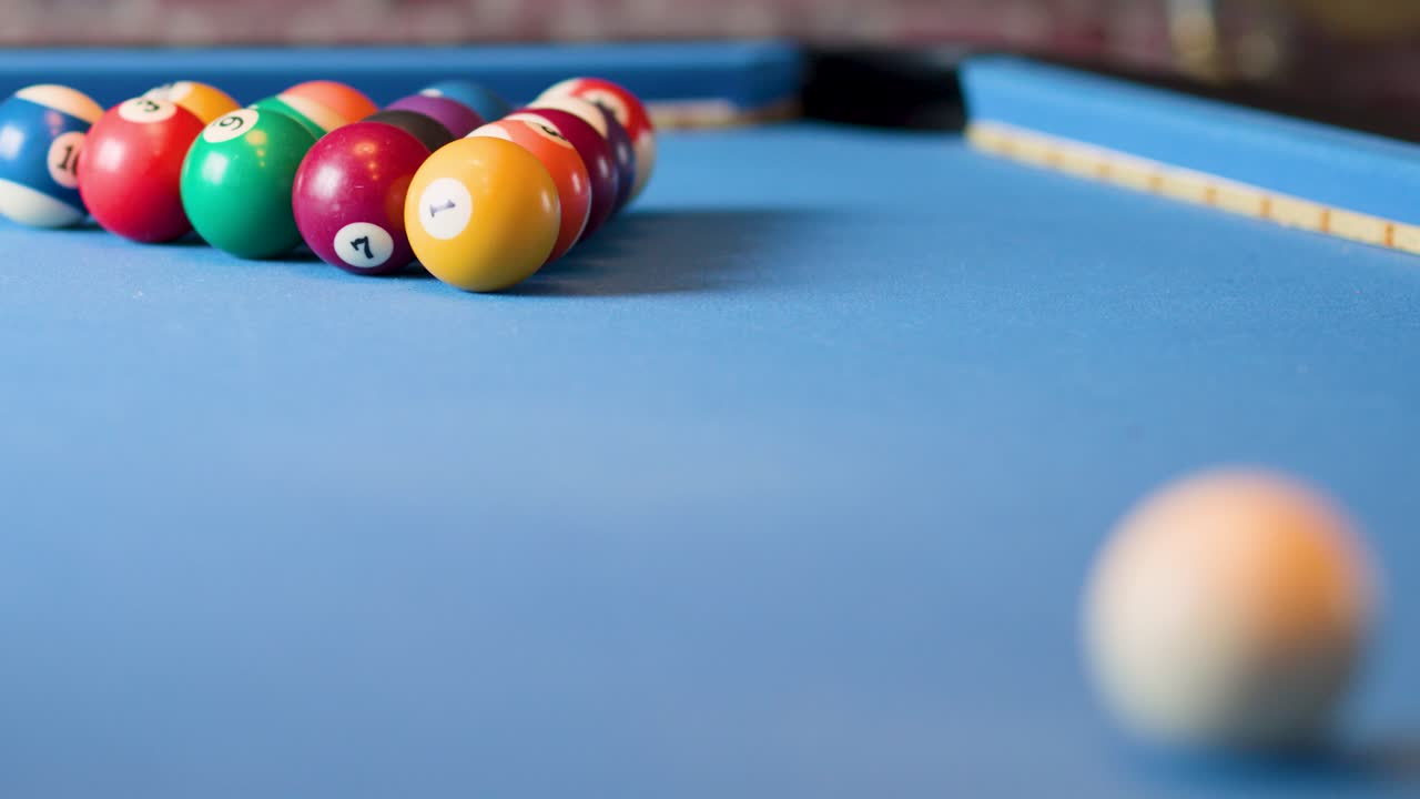 Colorful billiard balls scatter across blue felt pool table, shallow depth of field, natural lighting