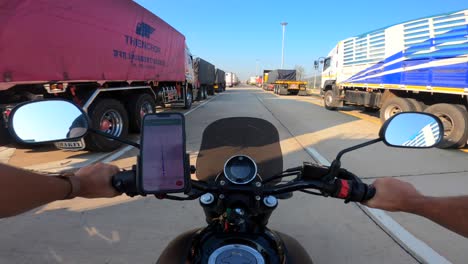 Standpunkt:-Kaukasischer-Mann,-Der-Google-Maps-IPhone-Verwendet-Und-Ein-Yamaha-Motorrad-Auf-Einer-Autobahn-Mit-Vielen-Geparkten-Sattelschleppern-In-Thailand-Fährt