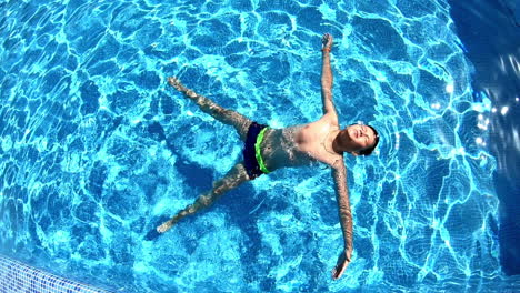 young boy in the swimming pool. teenager lying on his back on the water surface in a sunny day. blue clear water of a pool and a boy swimming.