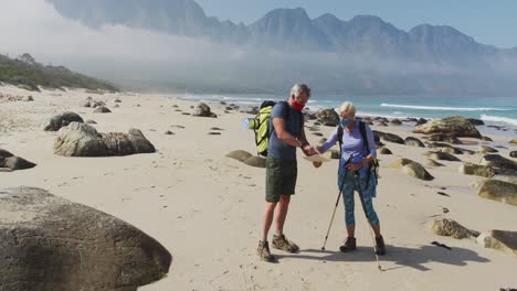 senior hiker couple wearing face masks with backpacks and hiking poles reading map while hiking