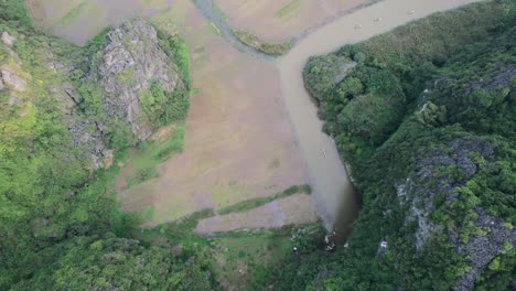 Sampan-boats-cruising-on-Ngo-Dong-River-gentle-current-between-striking-limestone-karsts-in-Ninh-Binh-Vietnam---top-down-aerial-view