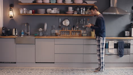 happy young man dancing in kitchen wearing pajamas smart phone coffee morning