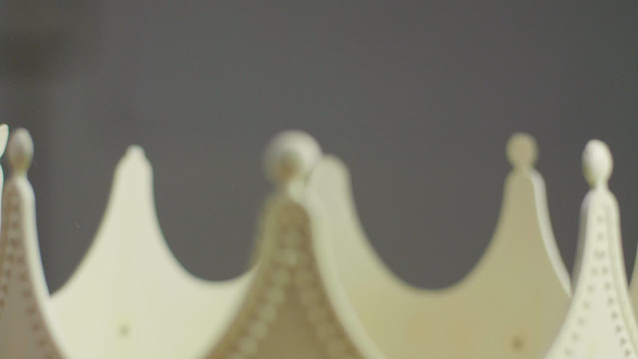 Close up of water flowing into a beige crown on a pedestal with ornaments and white pearl jewels with peaks jagged out of plastic. Smooth sliding camera movement. Shot in 4K.