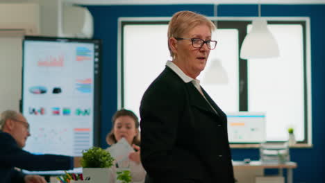 successful senior entrepreneur standing in front of meeting desk looking at camera