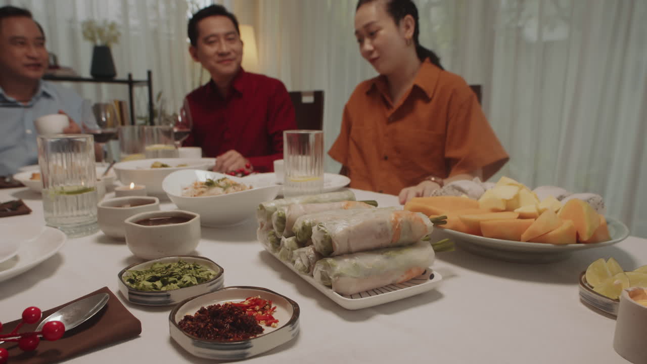 Young Woman Serving Spring Rolls on Table Dining with Family