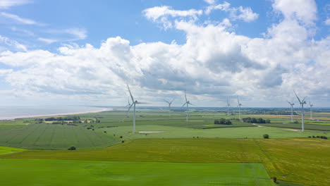 aerial hyperlapse of wind turbines and clouds with the wind making waves in the fields