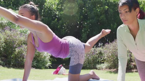 Happy-biracial-sisters-doing-yoga-and-stretching-in-garden,-in-slow-motion