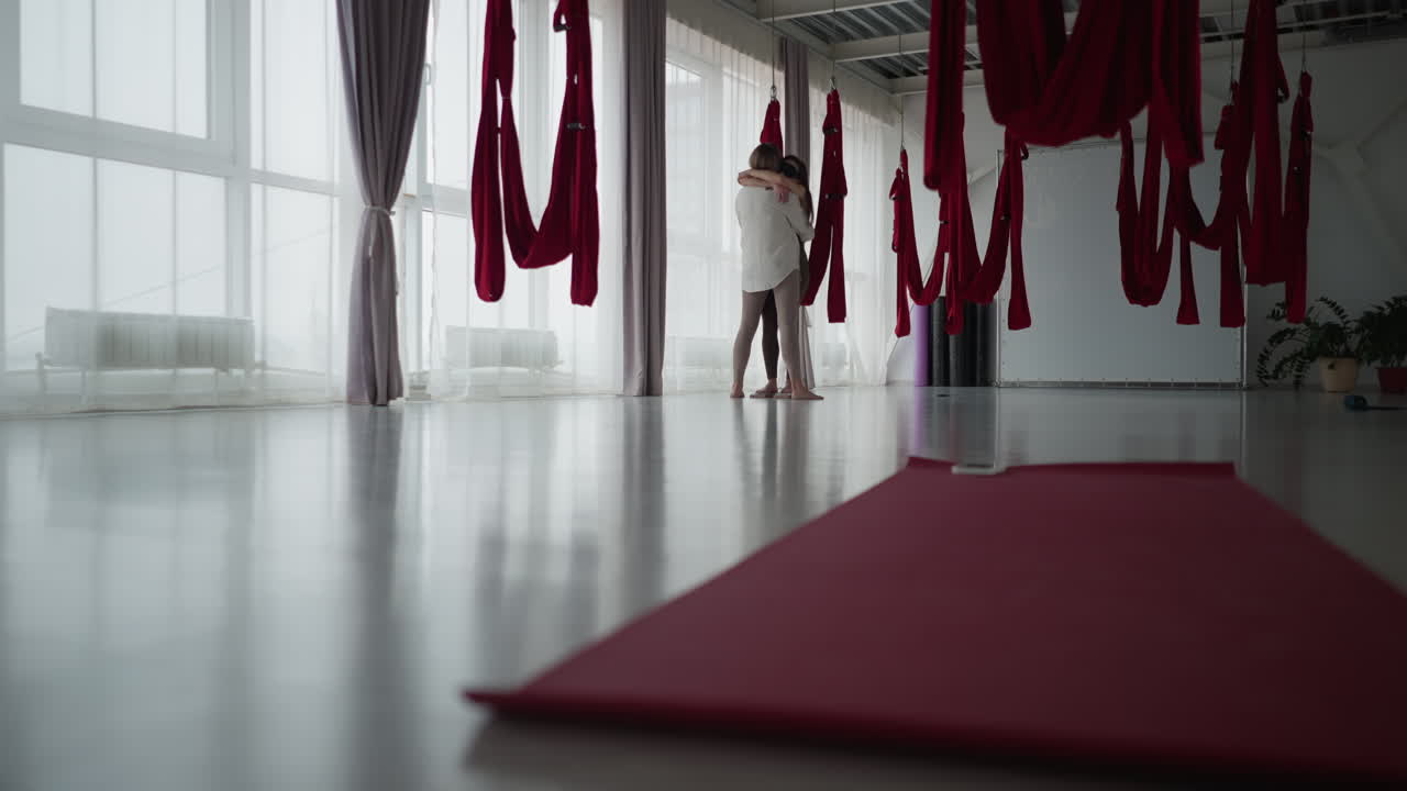 Wellness practitioner embraces partner standing barefoot on nail board in serene aerial silk studio, sharing emotional support under soft natural light, expressing mindful connection