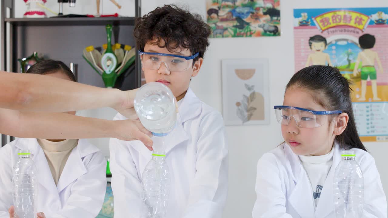 Asiatiske børn iført sikkerhedsbriller og laboratoriefrakker observerer et videnskabeligt eksperiment i et klasseværelse