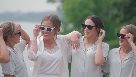 bridesmaids in white pajamas posing together outdoors by lake in slow motion