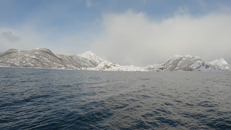 Bella-Escena-De-Un-águila-De-Cola-Blanca,-También-Conocida-Como-águila-Marina,-Buceando-Y-Pescando-En-El-Agua-Frente-A-Una-Hermosa-Montaña-Cubierta-De-Nieve,-Tiro-Panorámico