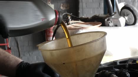 verter aceite nuevo en el motor del automóvil desde una botella usando un embudo sucio en un garaje