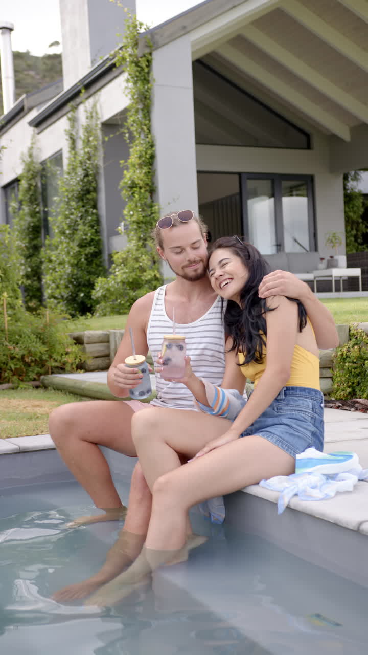 Video verticale: Relax a bordo piscina, coppia seduta insieme che si gode un drink a casa.