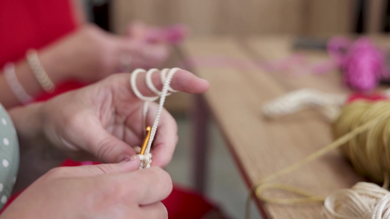 Primo piano di mani che lavorano all'uncinetto filato bianco con un uncinetto su un tavolo da lavoro, mostrando una tecnica tessile artigianale dettagliata, maestria e lavoro creativo