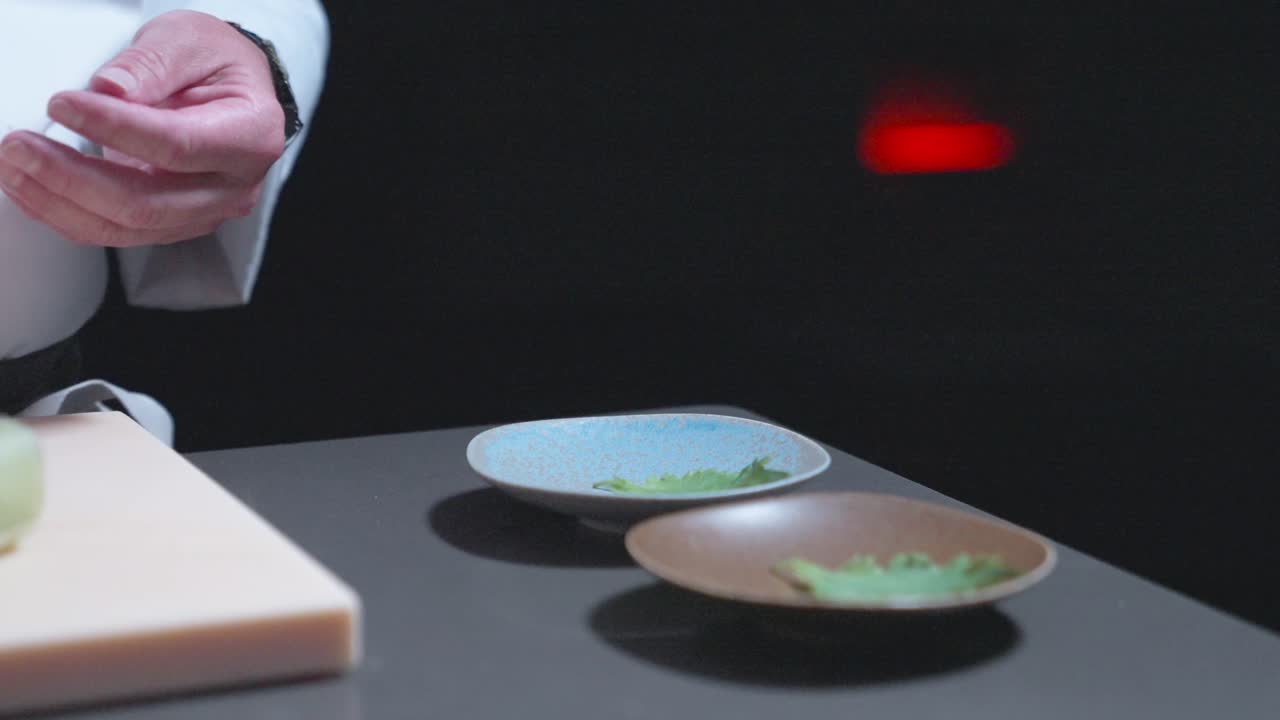 A sushi chef prepares sushi bowls, adding leaf decorations to enhance the presentation. Perfect for showcasing sushi preparation, Japanese cuisine, and food styling in culinary settings.