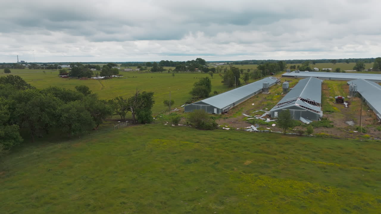 Establishing overview of broken long green houses and wide farmland under cloudy sky, Cherokee City, Arkansas, USA