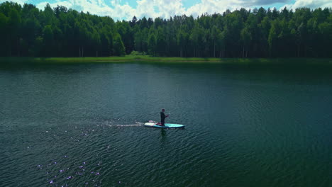 drone orbit of paddleboarder on lake amongst green trees