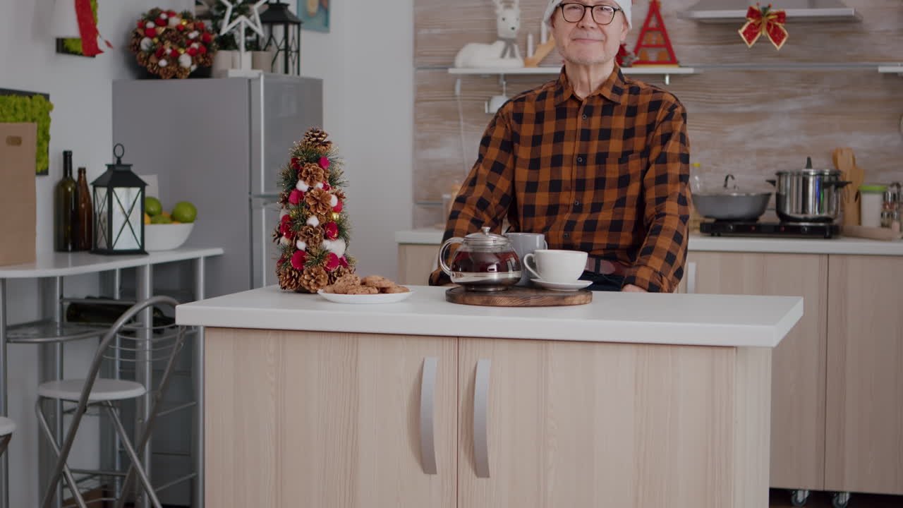 retrato de abuelo con sombrero de santa sentado en la cocina decorada con navidad