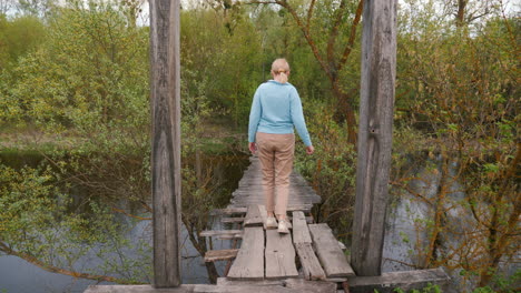 woman walking across an old wooden bridge in nature