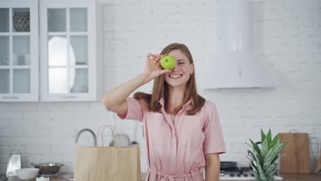 beautiful woman holding green apples on kitchen background. happy female closing her eyes by two fresh apples indoors. dieting concept.