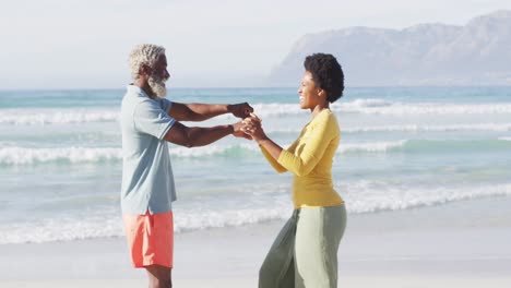 happy african american couple dancing and holding hands on sunny beach