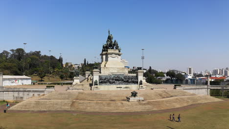 Toma-Aérea-Del-Monumento-A-La-Independencia-Que-Muestra-El-Fuego-De-La-Libertad-Que-Nunca-Se-Apaga-En-Primer-Plano-Y-El-Museo-Ipiranga-En-El-Fondo-De-La-Escena