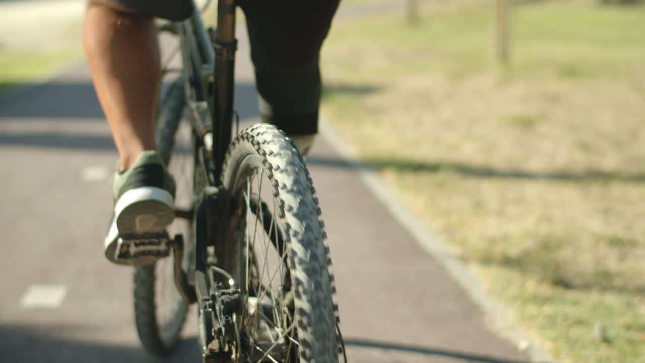 Primer plano de un hombre con pierna biónica andando en bicicleta en un parque de verano.