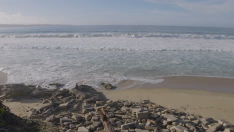 Slow-motion-shot-of-rolling-waves-on-a-rocky-shore-on-a-sunny-day-at-Monterey-Bay-California-Marina-State-Beach